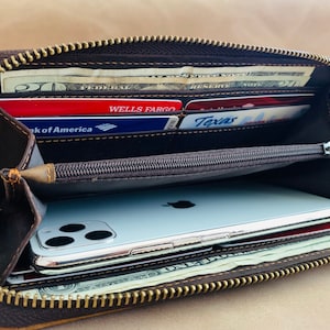 May include: A brown leather zippered wallet with a gold zipper. The wallet is open and contains cash, credit cards, and a smartphone.