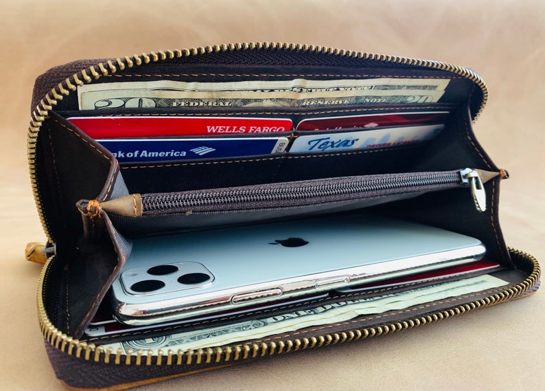 May include: A brown leather zippered wallet with a gold zipper. The wallet is open and contains cash, credit cards, and a smartphone.