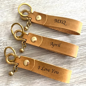 May include: Three brown leather keychains with brass key rings and charms. The keychains are personalized with the text "MXQ", "April", and "I Love You".