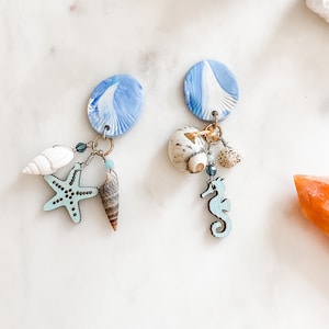 May include: A pair of blue and white swirl earrings with a seahorse, starfish, and seashells dangling from each earring.