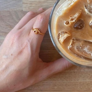 Peut inclure: Un verre de café glacé avec des glaçons et une paille. Le café est de couleur brun clair et les glaçons sont transparents. Le verre est sur une table en bois.