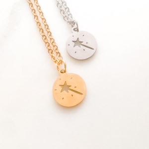 May include: Two necklaces with round pendants featuring a star and wand design. One necklace is gold-colored, the other is silver. Both have delicate chains. The pendants have a cut-out star and wand design.