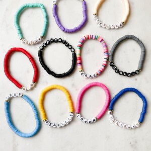 May include: Ten colorful bracelets with white beads spelling out the names of Taylor Swift albums: Speak Now, Evermore, Reputation, Folklore, 1989, Fearless, Lover, Midnights, Red, and Eras.