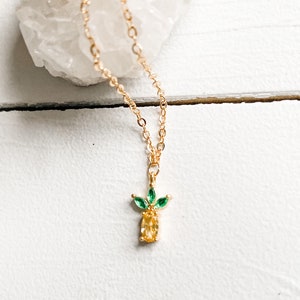 May include: A gold chain necklace with a small pineapple pendant. The pineapple is made of yellow and green cubic zirconia stones.