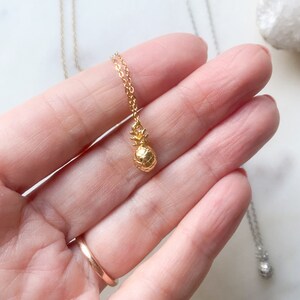 May include: A gold pineapple pendant necklace on a delicate gold chain. The pendant is small and detailed, with a textured pineapple design.