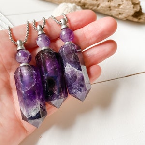 Könnte beinhalten: Drei Amethyst-Kristallspitzen-Halsketten mit silbernen Ketten und silbernen Kappen. Die Amethystkristalle sind tiefviolett mit weißen Einschlüssen.