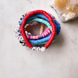 May include: A stack of colorful beaded bracelets with the word "RED" spelled out in white beads with gold lettering.
