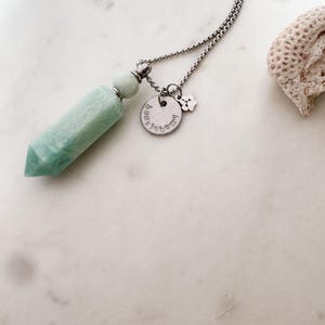 May include: A silver chain necklace with a light green crystal pendant and a silver charm with the text "Pawsitive" and a paw print.