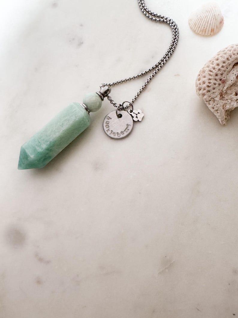 May include: A silver chain necklace with a light green crystal pendant and a silver charm with the text "Pawsitive" and a paw print.
