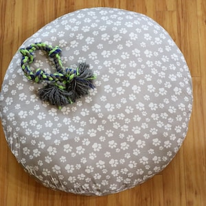 May include: A round gray dog bed with a white paw print pattern. A green and blue rope toy is on top of the bed.