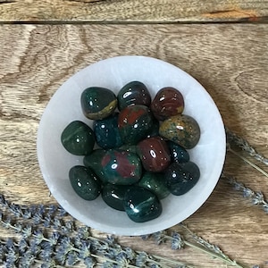 May include: A white bowl filled with polished green, red, and brown jasper tumbled stones.