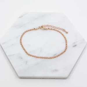 May include: A delicate gold-toned chain bracelet with a small, round link design. The bracelet has a lobster clasp closure and an extender chain.