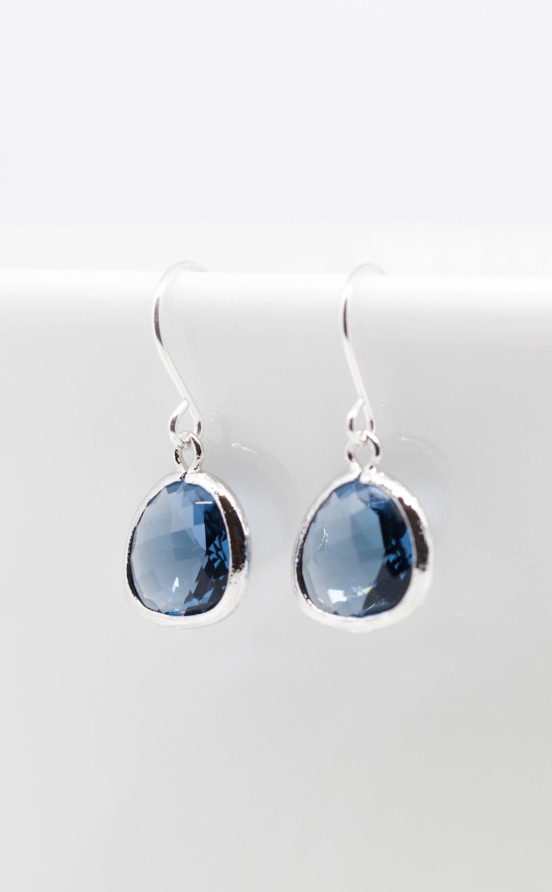 May include: A pair of silver dangle earrings with a light blue gemstone. The earrings have a simple design and are perfect for everyday wear.