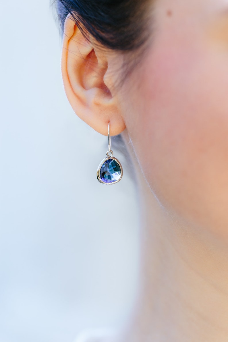 May include: Silver dangle earrings with a teardrop-shaped blue gemstone.