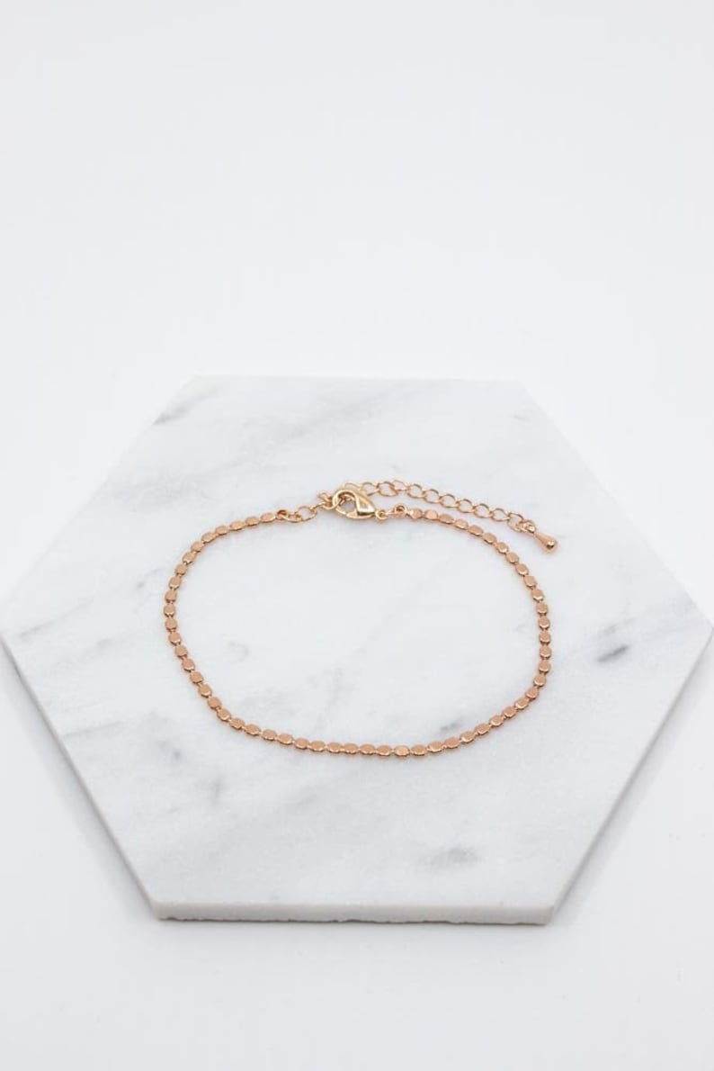 May include: A delicate gold-toned chain bracelet with a small, round link design. The bracelet has a lobster clasp closure and an extender chain.