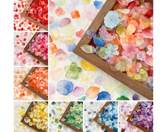 Puede incluir: Surtido de cuentas de resina de forma floral de colores en varios tonos de rosa, rojo, naranja, amarillo, verde, azul y morado. Las cuentas están dispuestas en recipientes separados, cada uno mostrando un color diferente.