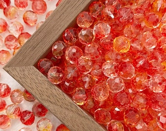 May include: A close-up of a wooden box filled with red and orange glass beads. The beads are faceted and have a clear, translucent finish. The beads are scattered around the box, creating a colorful and textured display.