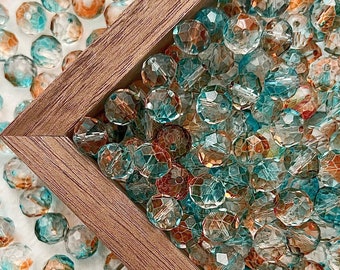 May include: A close-up of a wooden frame filled with teal and amber glass beads. The beads are arranged in a random pattern and are all the same size. The frame is sitting on a white surface.