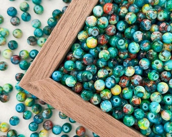 May include: A close-up of a wooden box filled with colorful, round, glass beads. The beads are a mix of teal, green, blue, yellow, and red colors. The beads are scattered around the box.