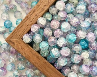 May include: A wooden box filled with iridescent blue and purple glass beads. The beads have a textured, faceted surface and are scattered around the box.
