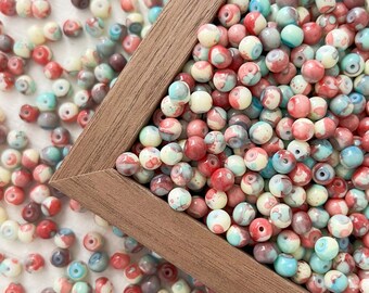 May include: A close-up of a wooden frame filled with colorful, round beads. The beads are a mix of white, red, and blue with swirling patterns. The beads are scattered around the frame on a white surface.
