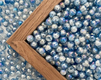 May include: A wooden frame filled with iridescent blue glass beads. The beads are round and have a slight shimmer to them.