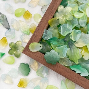 May include: A wooden box filled with green, blue, and yellow translucent flower and leaf shapes. The box is surrounded by similar shapes on a white surface.