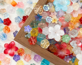 May include: A close-up of a wooden box filled with colorful flower-shaped beads. The beads are made of glass and have a variety of colors, including pink, blue, green, yellow, and red. The beads are arranged in a random pattern and are surrounded by a wooden frame.