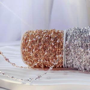 May include: Two spools of decorative chain, one gold and one silver. The gold chain is adorned with tiny pink pearls. The silver chain also features small pearls. A length of silver chain is visible.