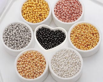 May include: A collection of small, round, metallic-finish beads organized into six white circular bowls and one central heart-shaped bowl. The beads are sorted by color, featuring gold, rose gold, silver, and black tones in a polished finish.