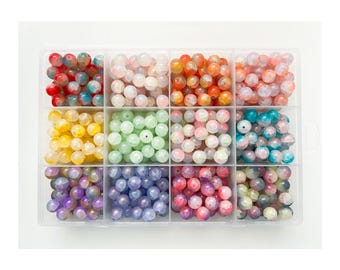 Può includere: Un organizer di plastica trasparente pieno di perline rotonde e colorate. Le perline sono di vari colori, tra cui rosso, arancione, giallo, verde, rosa, viola e blu. Le perline sembrano essere di vetro o di un materiale simile.