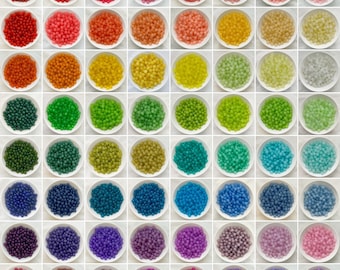 May include: A grid of small, round, colorful beads in white bowls. The beads are arranged in rows and columns, showcasing a wide spectrum of colors, including red, orange, yellow, green, blue, and purple. The beads appear to be uniform in size and shape.