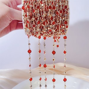 May include: A spool of gold chain with red and clear glass beads. The chain is made of small, round beads that are connected by a thin gold chain.