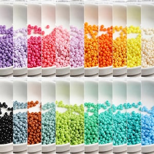 Peut inclure: Une collection de petites perles de rocaille opaques, rondes, disposées en vingt colonnes verticales, chacune présentant une couleur unie distincte, notamment des nuances de violet, rose, orange, jaune, blanc, noir, gris, marron, vert et bleu.
