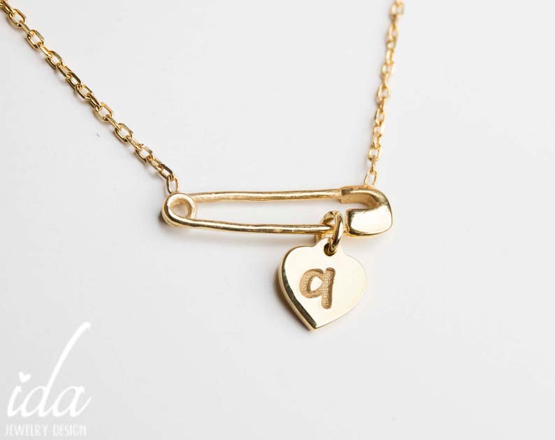 May include: A gold necklace with a safety pin charm and a heart pendant with the letter "q" engraved on it.