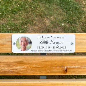 May include: A memorial plaque on a wooden bench. The white plaque features a photo of a woman, the text "In Loving Memory of Edith Morgan," and dates 12.09.1948 - 23.05.2022. The inscription reads, "Always in our thoughts, forever in our hearts."