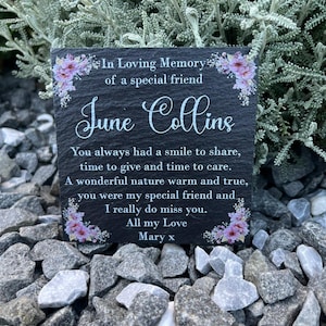 May include: A black slate memorial plaque with floral accents and the inscription "In Loving Memory of a special friend June Collins." The text includes a heartfelt message and is surrounded by decorative flowers.