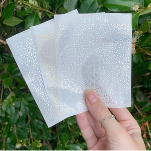 May include: Three sheets of clear sticker paper with a repeating pattern of small silver glitter dots. The top sheet has the text "Busy B Prints" printed in black.