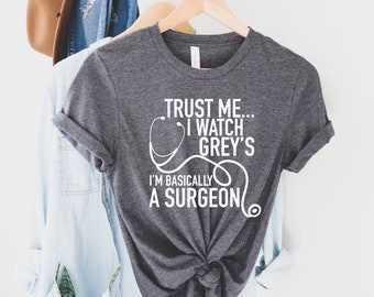 May include: A dark gray t-shirt with a white graphic that says "Trust me... I watch Grey's I'm basically a surgeon" with a stethoscope graphic.