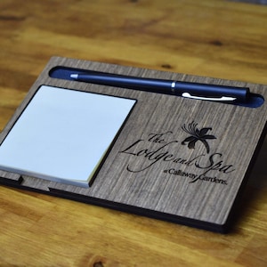 May include: A wooden desk organizer with a notepad, pen holder, and engraved logo that reads "The Lodge and Spa at Callaway Gardens."