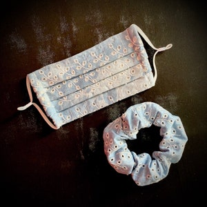 May include: A light blue cotton face mask with white embroidery and a matching light blue scrunchie.