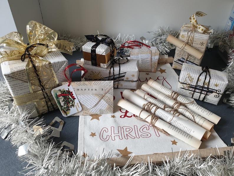 May include: A collection of Christmas gifts wrapped in vintage book pages, adorned with ribbons, tags, and twine. Some gifts have gold accents and snowflake designs. A fabric banner with "Let it Christmas" is also present.
