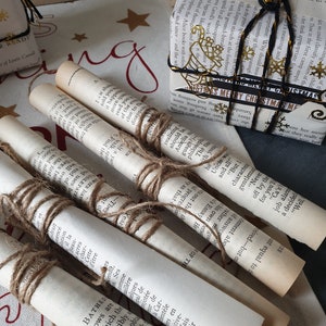 May include: Several rolled-up book pages tied with twine, alongside wrapped gifts. The gifts are wrapped in book pages and decorated with gold accents and black ribbon. The scene evokes a vintage, literary, and festive theme.