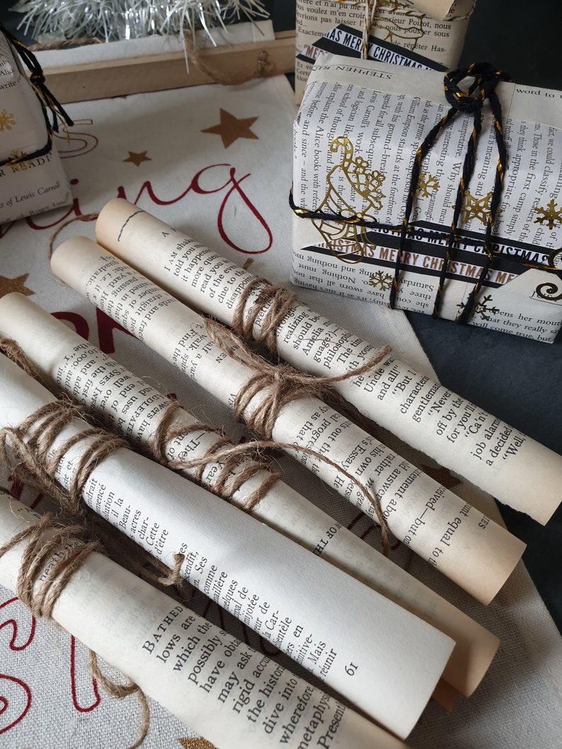May include: Several rolled-up book pages tied with twine, alongside wrapped gifts. The gifts are wrapped in book pages and decorated with gold accents and black ribbon. The scene evokes a vintage, literary, and festive theme.