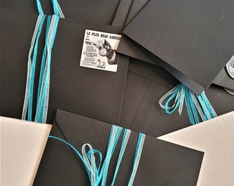 May include: A collection of black envelopes tied with turquoise and white ribbons. Some envelopes have small vintage-style labels and a silver wax seal with a heart design. The envelopes are arranged on a light-colored surface.