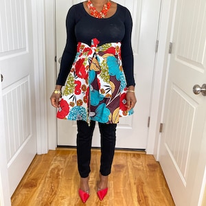 Peut inclure: Une femme portant une chemise noire à manches longues avec une jupe portefeuille à imprimé floral coloré. La jupe a un motif floral brun, blanc, bleu, rouge et jaune. Elle porte des talons hauts rouges.