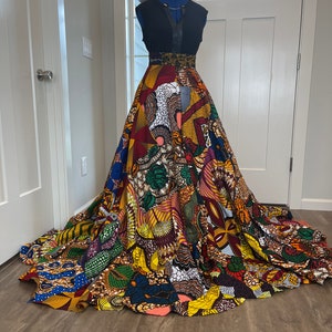 May include: A long, colourful maxi skirt with a black sleeveless top. The skirt is made of a patchwork of different African print fabrics in shades of yellow, red, blue, green, and brown. The skirt has a fitted waist and a full, flowing skirt.