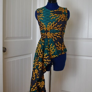 Puede incluir: Una blusa sin mangas con un dobladillo alto-bajo. La blusa está hecha de una tela verde y amarilla con un patrón geométrico. La tela tiene un fondo negro con lunares blancos.