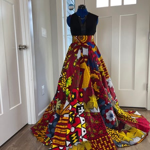 May include: A long, colourful skirt with a patchwork design featuring red, yellow, and blue patterns. The skirt is made of a fabric with a bold, geometric print. The skirt is being displayed on a mannequin.