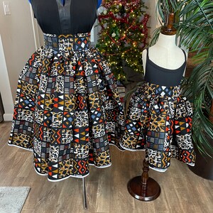 May include: Two black sleeveless tops with a high-waisted skirt featuring a colourful geometric and animal print pattern. The skirt is pleated and has a white trim.